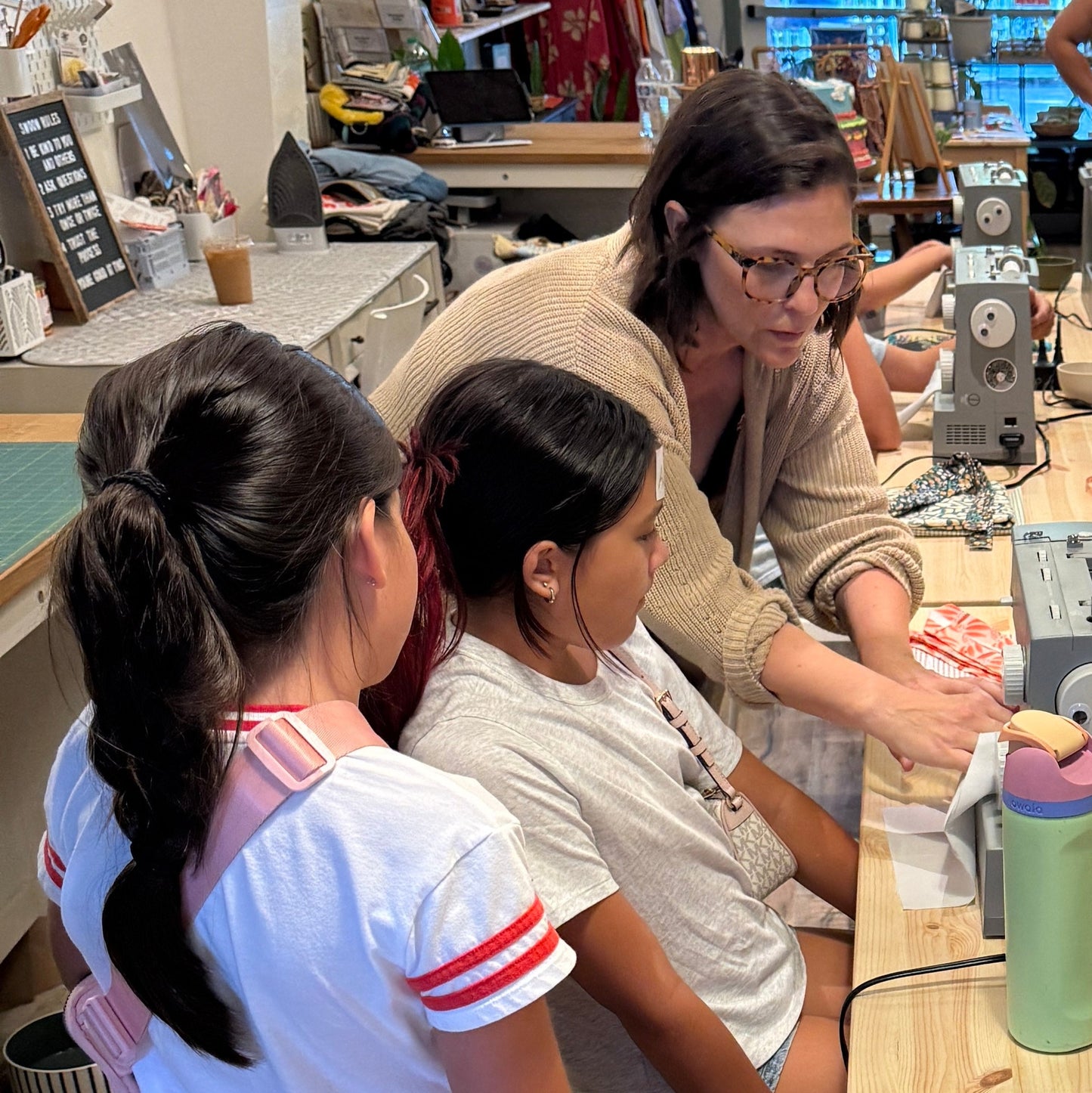 children getting a sewing lesson in a workshop from an adult teacher